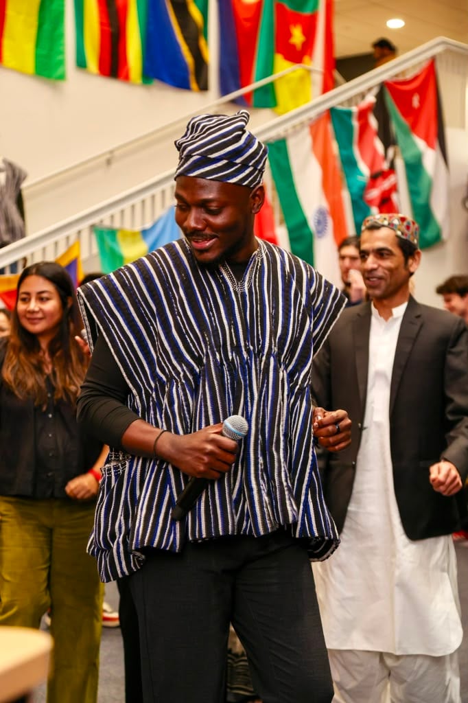 Terrick holding a microphone in a Ghanaian smock, leading a crowd at an international festival